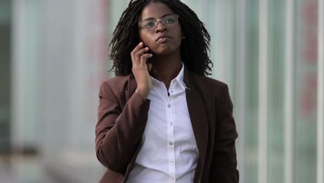 Concentrated-businesswoman-with-dreadlocks-talking-on-smartphone